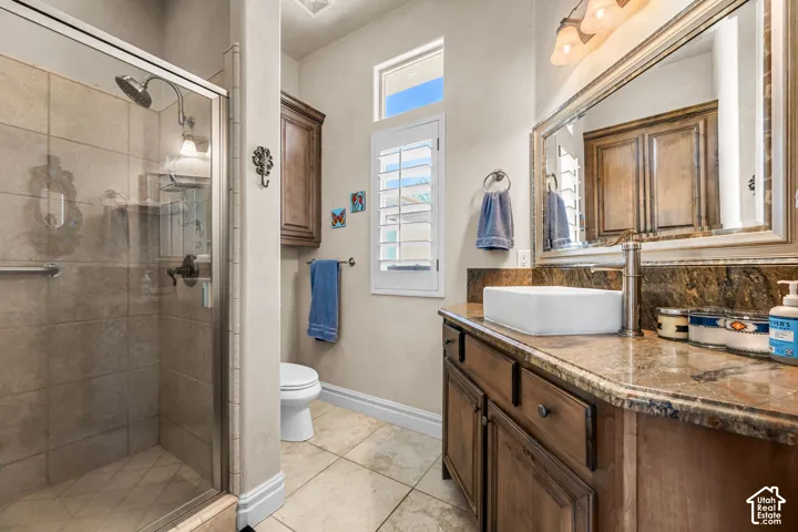 Walk-in shower with glass enclosure, brown vanity with stone-finish countertop, rectangular vessel sink, and an upper window with louvered shutters