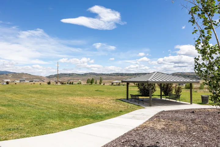 Expansive green space featuring a covered pavilion with seating, mature landscaping, and a paved pathway