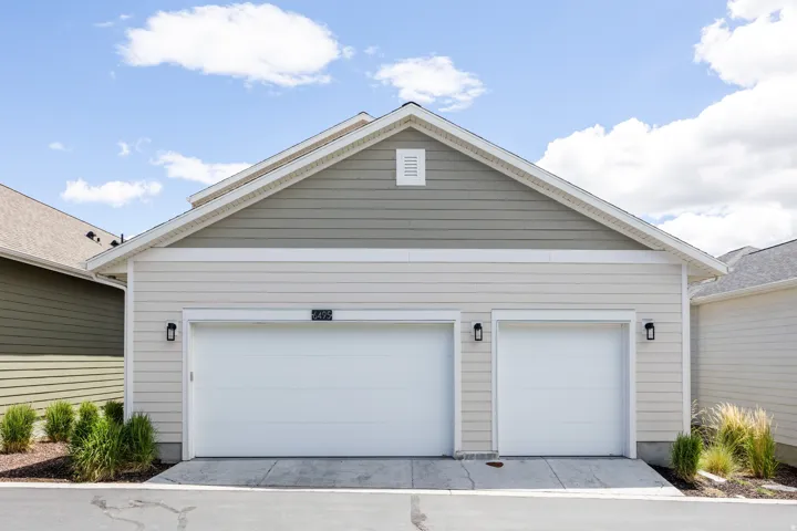 Two-car garage with white doors, light-colored horizontal siding, and a contrasting upper gable with green horizontal siding