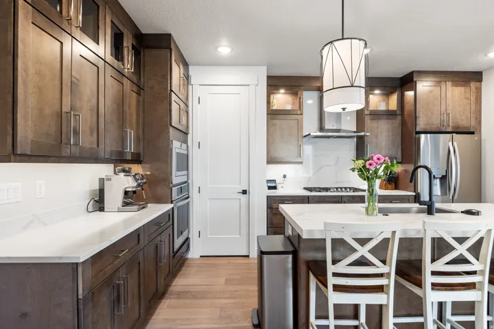 Modern kitchen with dark wood-finish cabinetry, white countertops, built-in stainless steel appliances, and a central island with a sink