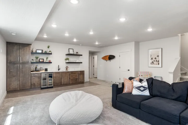 Recreation room featuring recessed lighting, a wet bar with integrated beverage refrigeration, floating wood shelves, and wood-finish cabinetry