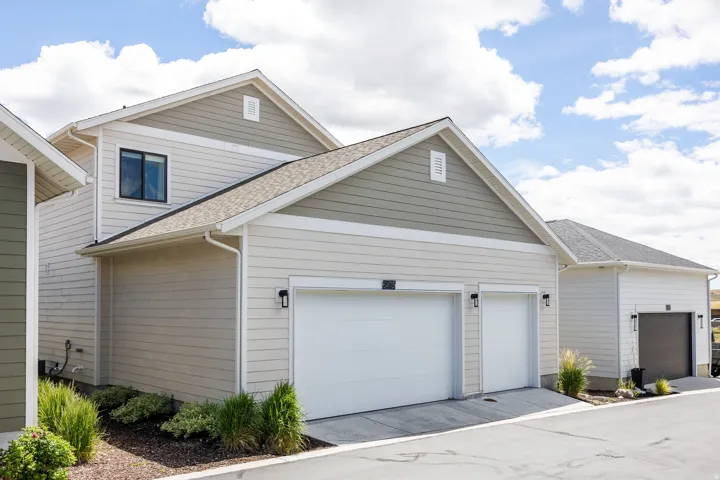 Two-car garage with white doors, exterior lighting, and a paved driveway