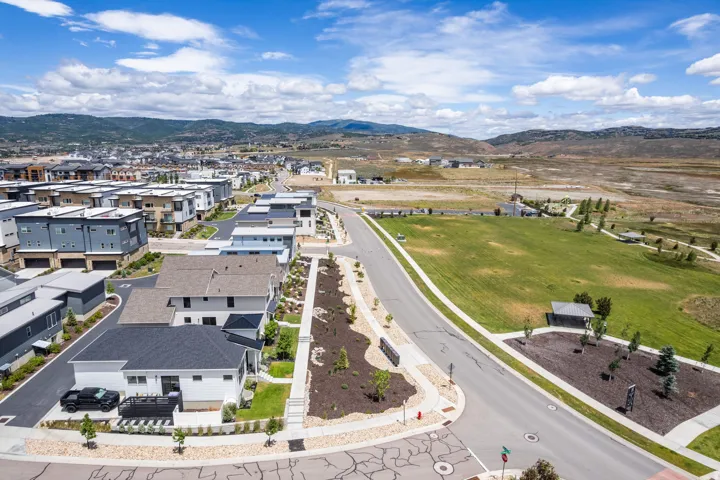 Modern residential development with a mountain backdrop, a large community green space, paved pedestrian pathways, and structured landscaping