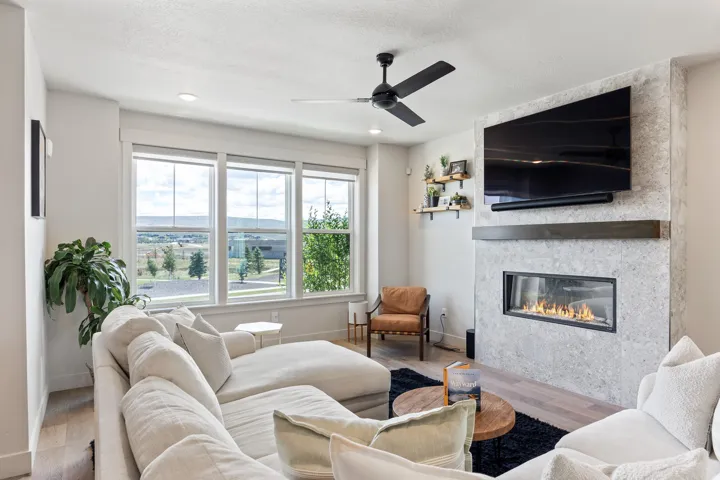 Contemporary living area featuring a linear gas fireplace with a stone-finish surround, a dark wood-finish mantel, and wood-finish flooring