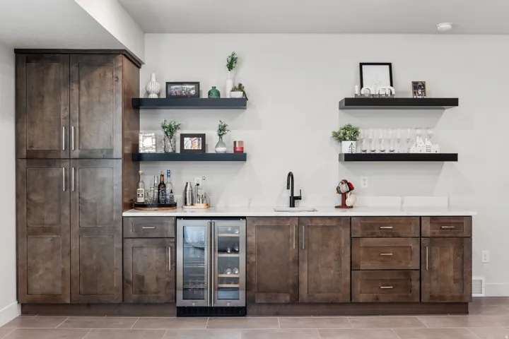 Built-in cabinetry with a wood-finish, stone countertops, integrated beverage cooler, matte black sink faucet, and floating wall shelves