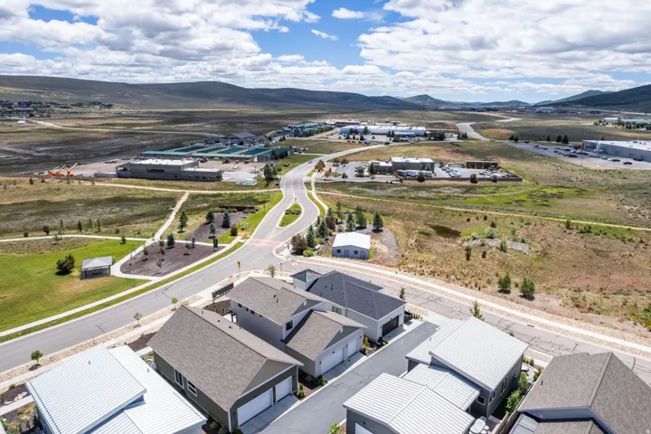 Aerial perspective showcasing a residential development with varied rooflines, paved roads, nearby commercial structures, and distant mountainous terrain