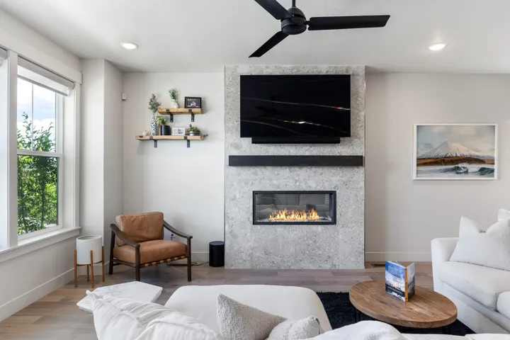 Integrated gas fireplace with a stone-finish surround, black ceiling fan, recessed lighting, wood-finish flooring, and large windows