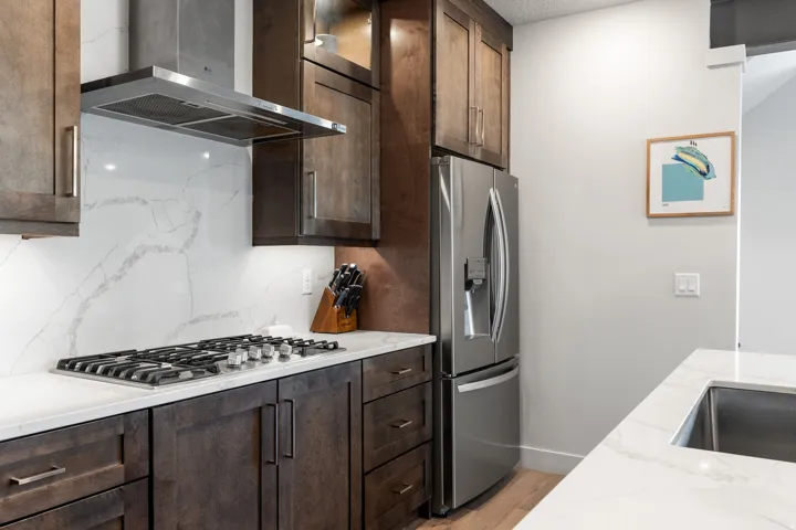 Kitchen featuring dark wood-finish cabinetry, stainless steel appliances, a gas cooktop, a stainless steel range hood, and white countertops with a subtle gray veining