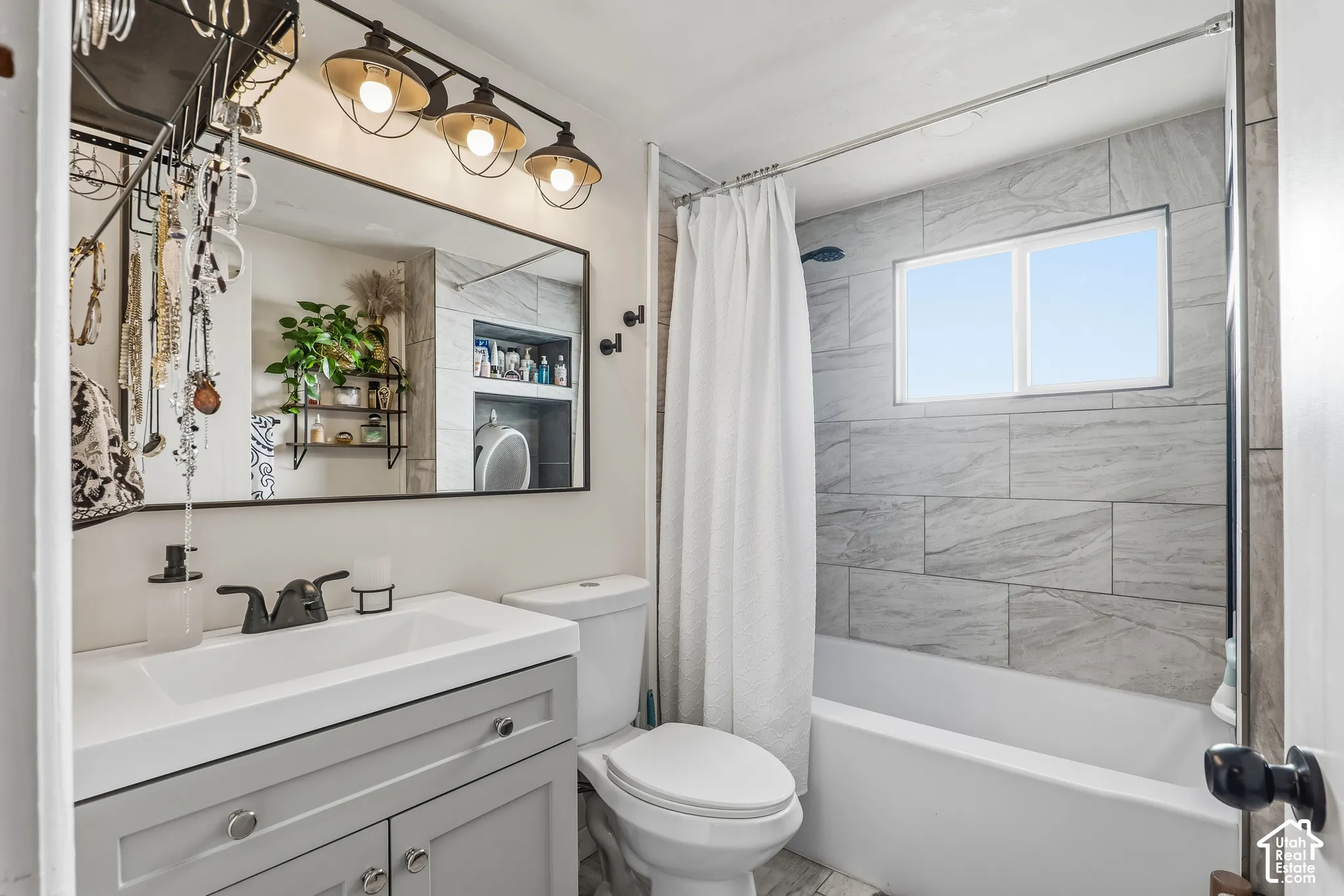 Vanity with a rectangular sink and matte black faucet, framed mirror, modern overhead lighting, tiled shower surround, and built-in window