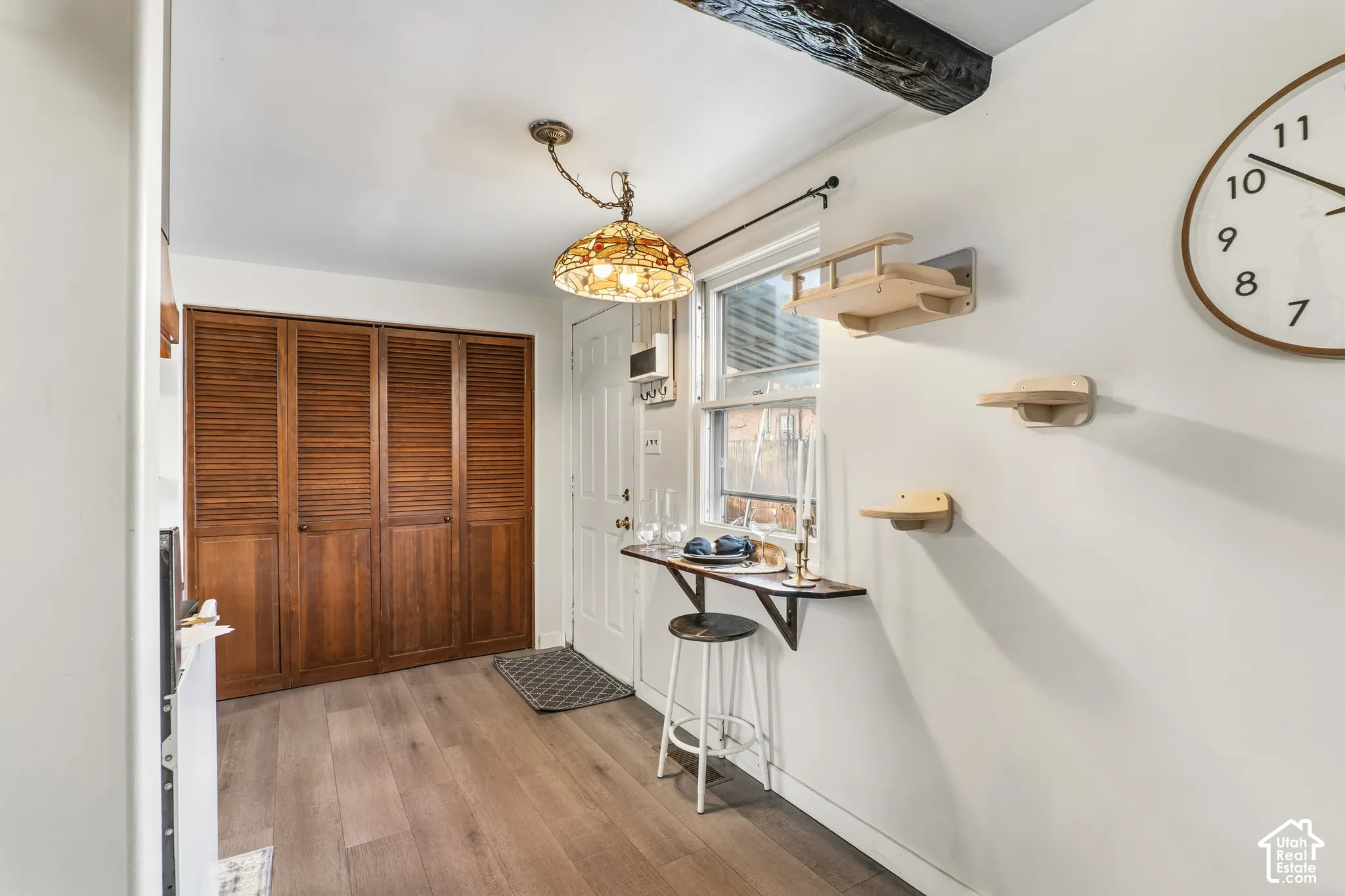 Wood-finish flooring, louvered bi-fold doors, exposed wood beam, window, and wall-mounted shelving