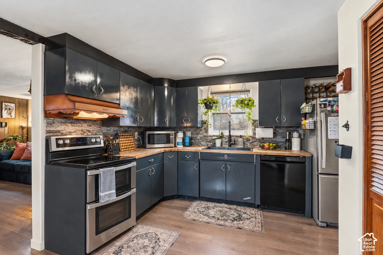 Original photo shows the old stove, this was altered to show the new stove. Kitchen featuring wood-finish flooring, dark cabinetry, stainless steel oven, and a tiled backsplash