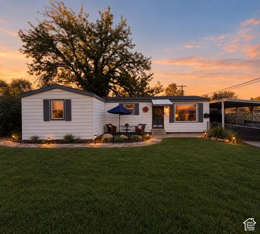 White siding exterior with dark shutters, front yard with manicured lawn, stone-edged landscaping beds, and a paved walkway