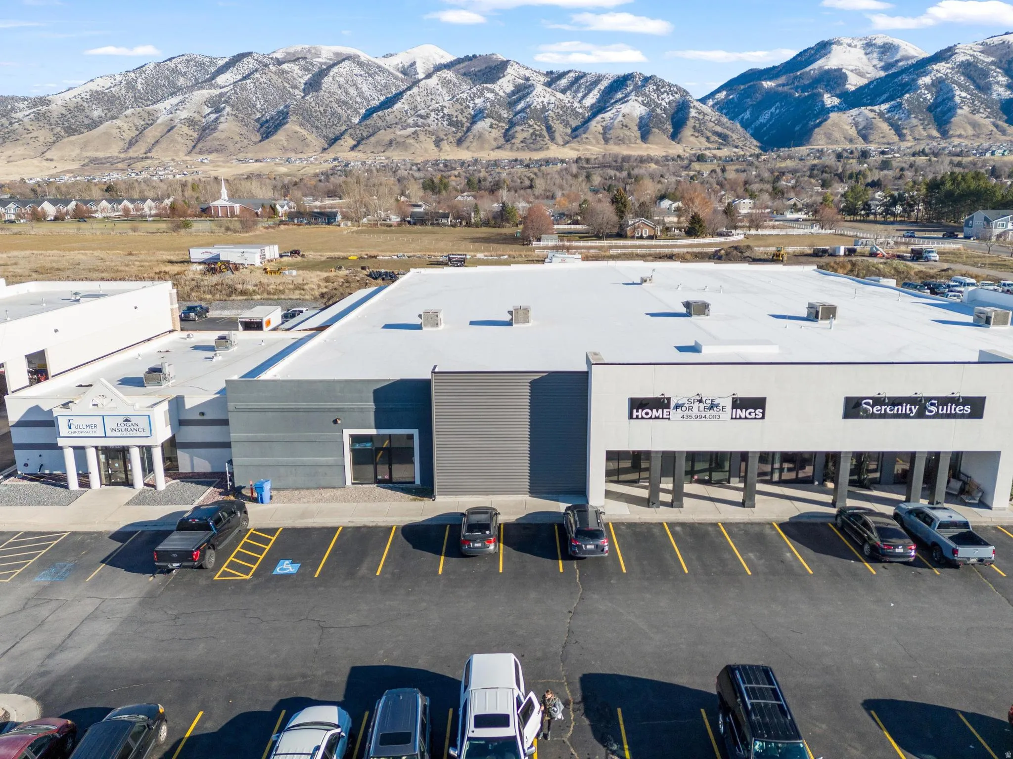 Commercial building with multiple storefronts, a large asphalt parking area, and a flat white roof