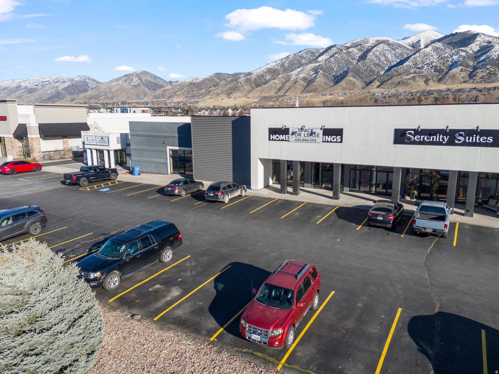 Modern commercial building with large storefront windows, dedicated parking, and mountain scenery