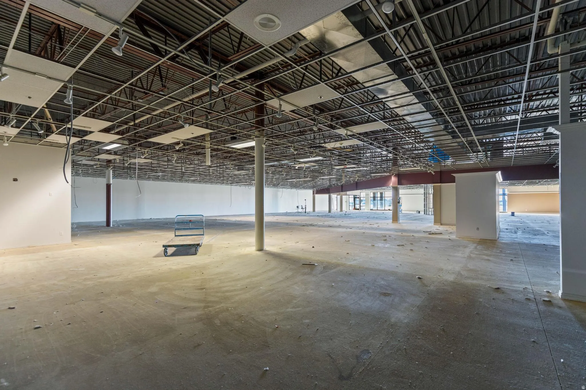 Expansive open-concept interior featuring exposed ceiling grids, partial drop ceiling panels, exposed ductwork, and concrete flooring