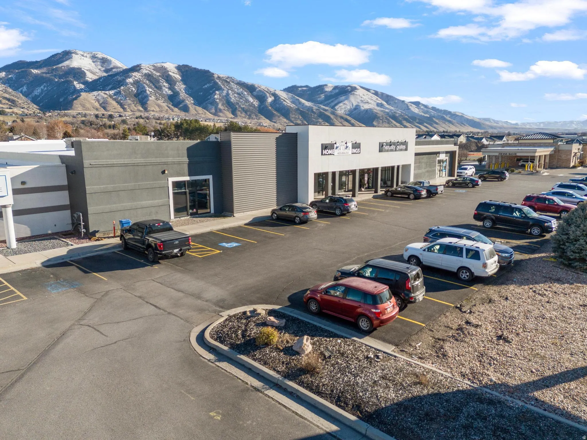 Commercial building featuring a paved parking lot, multiple storefronts, and a mountain backdrop