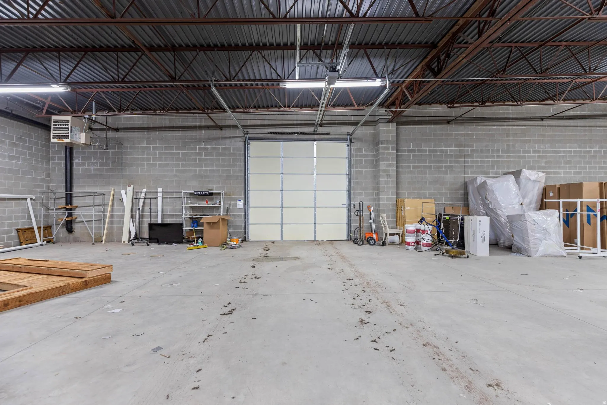 Exposed structural ceiling, concrete block walls, overhead fluorescent lighting, concrete flooring, and a large roll-up door