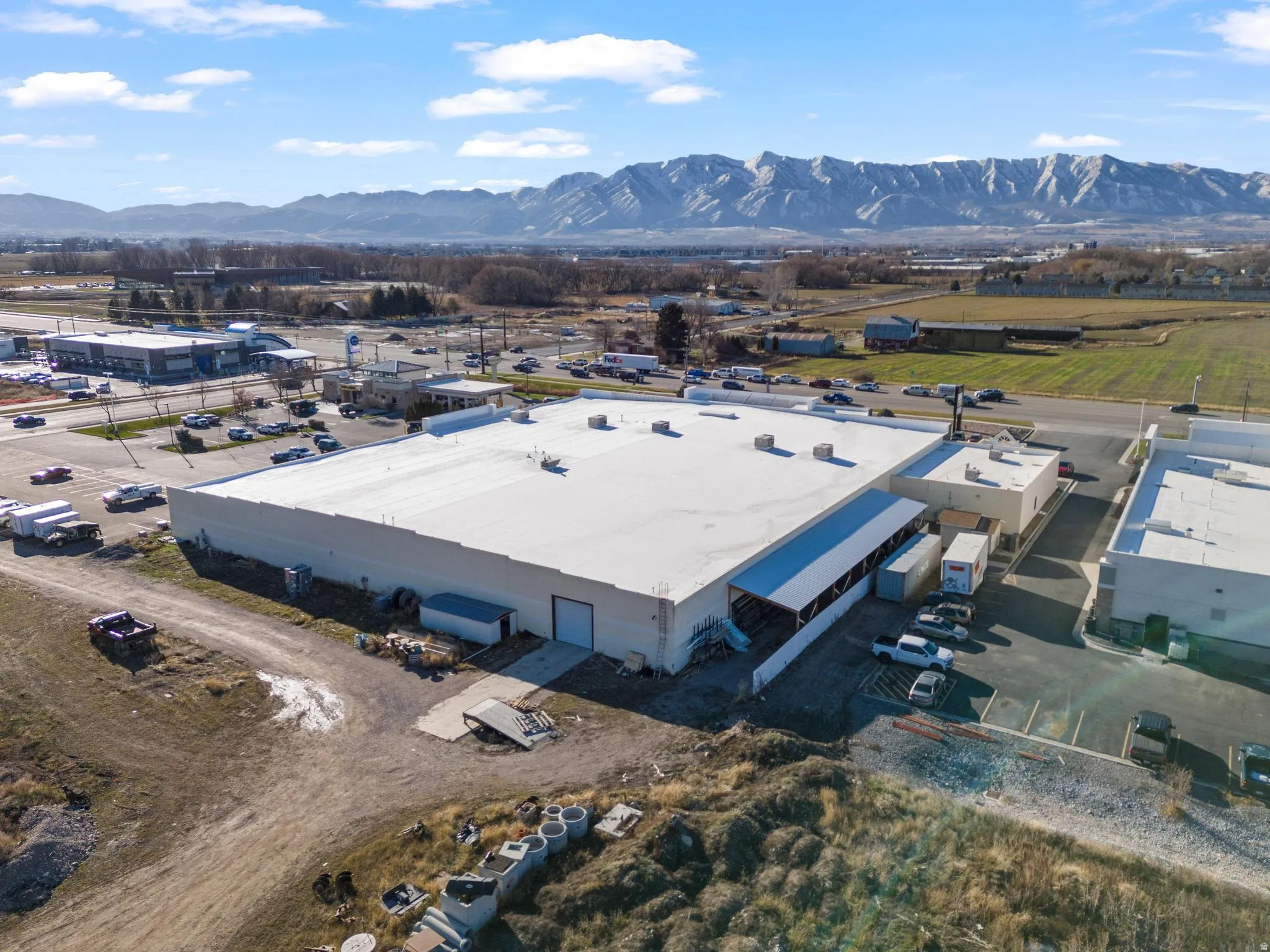 Industrial building featuring a white flat roof, multiple large bay doors, and extensive surrounding paved areas