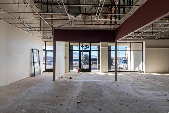 Exposed ceiling grid with recessed lighting, large storefront windows, partial interior walls, and concrete flooring