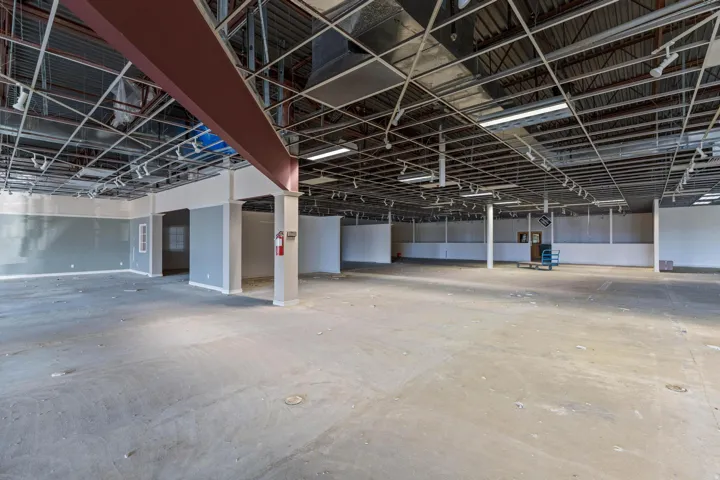 Spacious commercial interior featuring exposed ceiling framework, multiple support columns, and track lighting