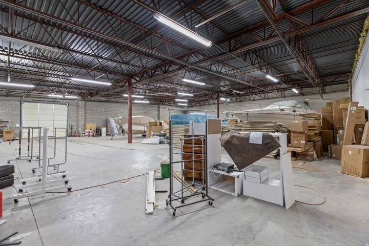 Expansive warehouse space featuring a high corrugated ceiling, exposed steel trusses, concrete block walls, and overhead fluorescent lighting