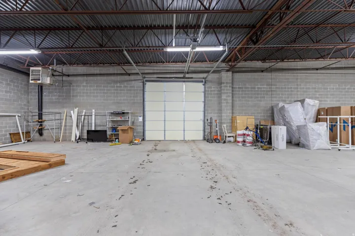 Exposed structural ceiling, concrete block walls, overhead fluorescent lighting, concrete flooring, and a large roll-up door