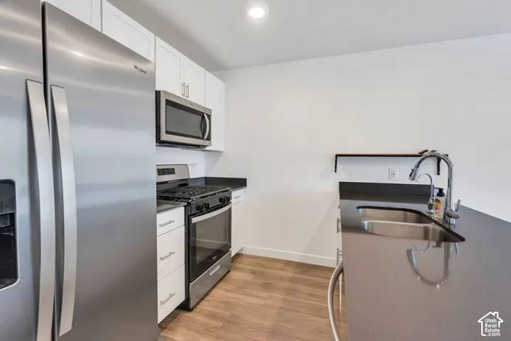 Kitchen featuring stainless steel appliances, white cabinetry, dark countertops, and wood-finish flooring