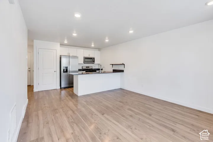 Kitchen with stainless steel appliances, white cabinetry, dark countertops, and wood-finish flooring