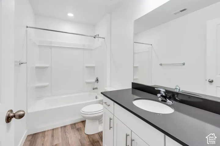 Bathroom featuring a full vanity with dark countertop, an undermount sink with chrome fixtures, white cabinetry, a built-in tub and shower combination, and wood-finish flooring