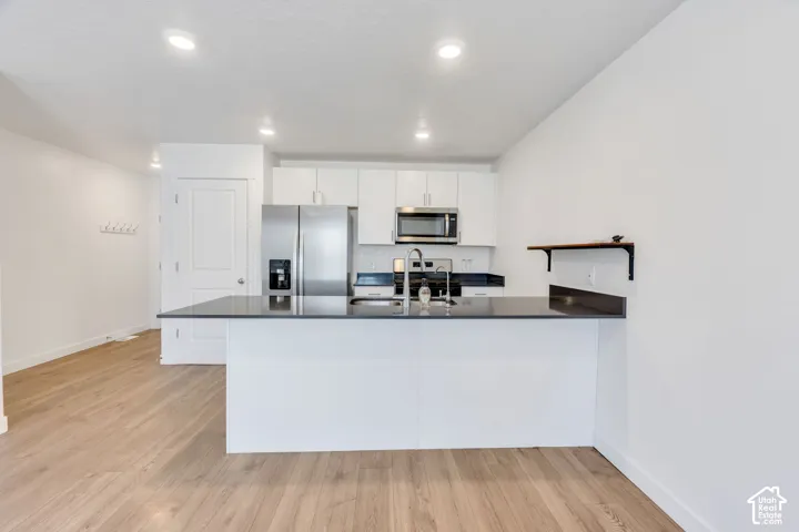 Open-concept kitchen with a breakfast bar, stainless steel appliances, white cabinetry, recessed lighting, and wood-finish flooring