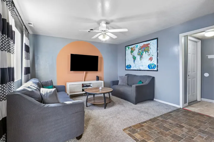 Carpeted living area with a ceiling fan light fixture and a media console with a light wood-finish top