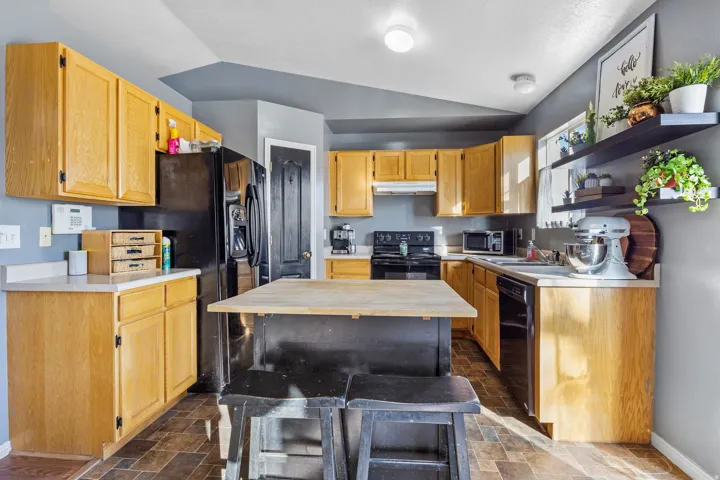 Kitchen featuring wood-finish cabinetry, light-toned countertops, black appliances, a central island, and wood-finish flooring