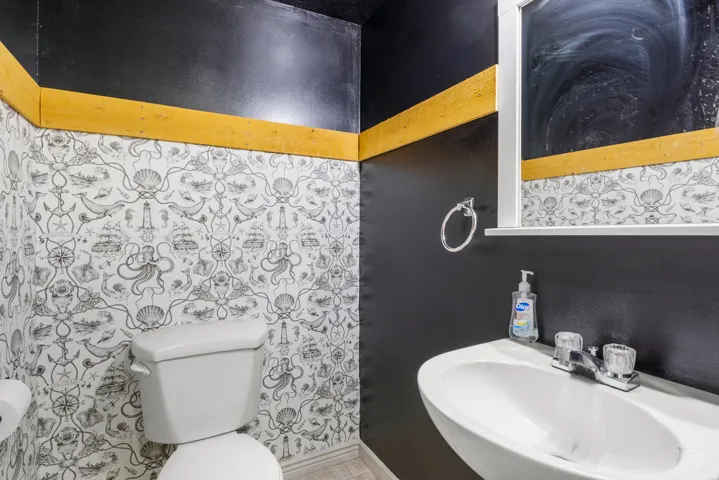 Pedestal sink with dual-handle faucet, wall-mounted mirror, and decorative wallpaper
