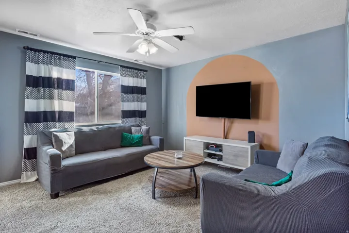 Carpeted living area featuring a ceiling fan, a window, and a built-in media console