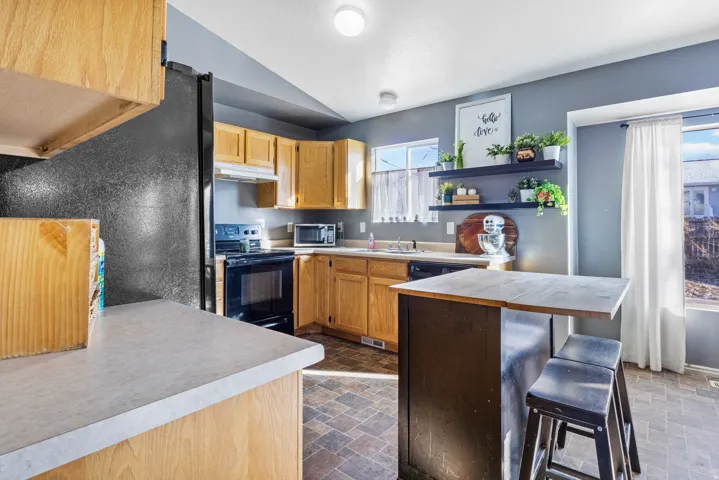 Kitchen featuring wood-finish cabinetry, black appliances, built-in shelving, and a peninsula with seating