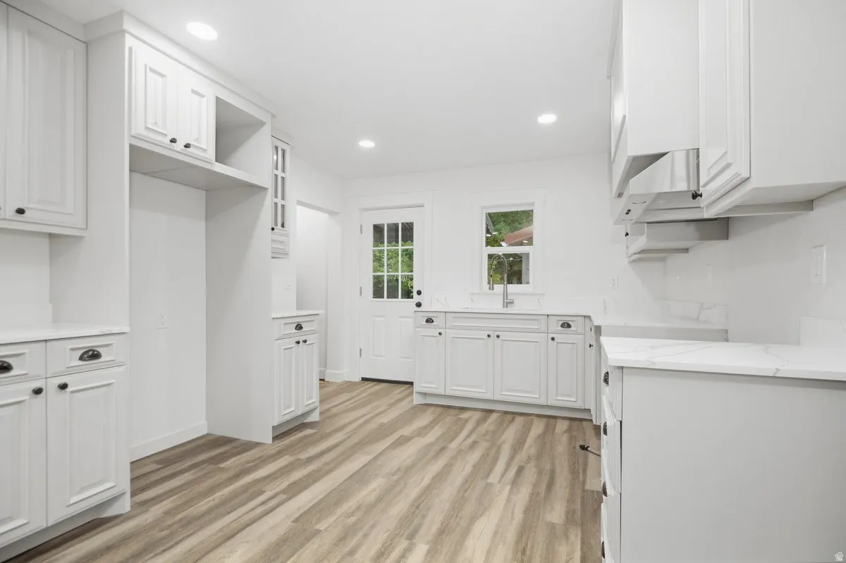 White shaker-style cabinetry, wood-finish flooring, recessed lighting, white countertops, and a white subway tile backsplash