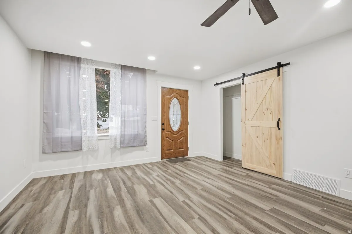 Wood-finish flooring throughout, with a recessed lighting package, a ceiling fan, and a natural wood barn door