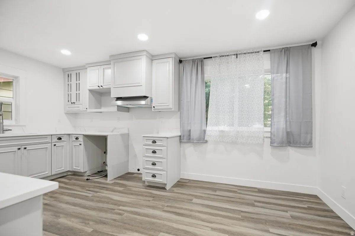 Kitchen featuring white shaker-style cabinetry, a built-in range hood, white countertops, wood-finish flooring, and recessed lighting