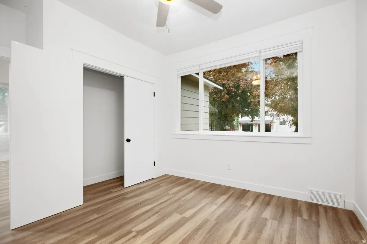 Wood-finish flooring, white walls, double-door closet, ceiling fan, and large window