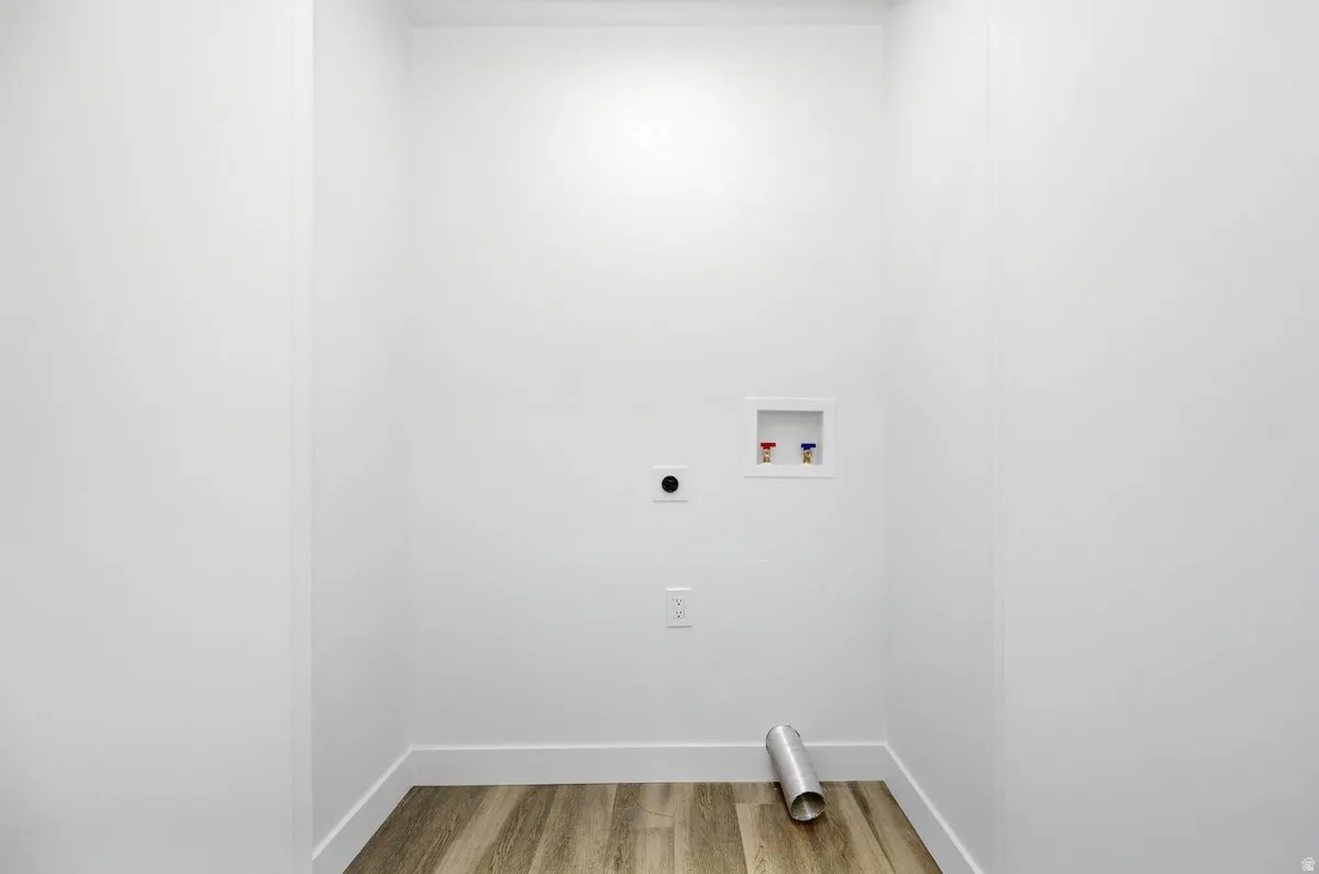 Dedicated utility area featuring white walls, wood-finish flooring, and plumbing connections for appliances