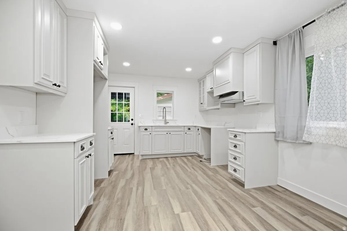 White cabinetry with dark hardware, wood-finish flooring, recessed lighting, and a subway tile backsplash