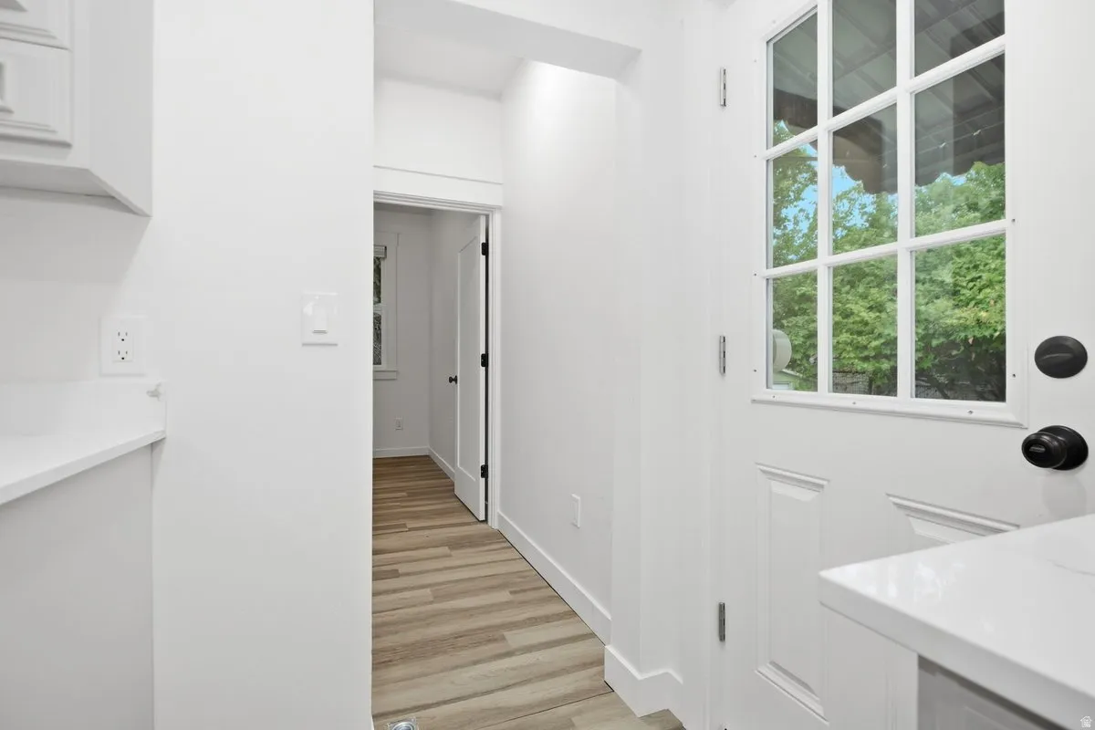 White shaker-style cabinetry with white countertop, wood-finish flooring, and a white paneled door with window-panes and black hardware