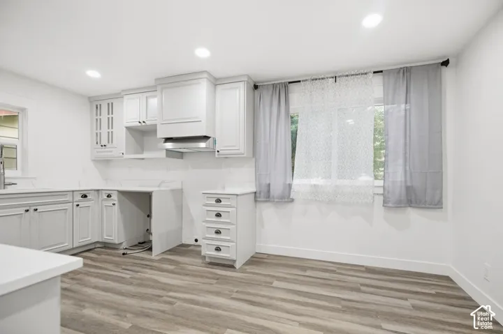 Kitchen featuring white shaker-style cabinetry, a built-in range hood, white countertops, wood-finish flooring, and recessed lighting