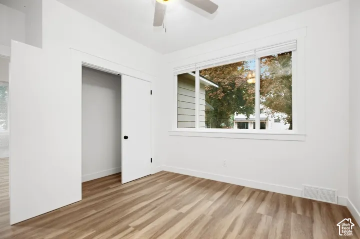 Wood-finish flooring, white walls, double-door closet, ceiling fan, and large window