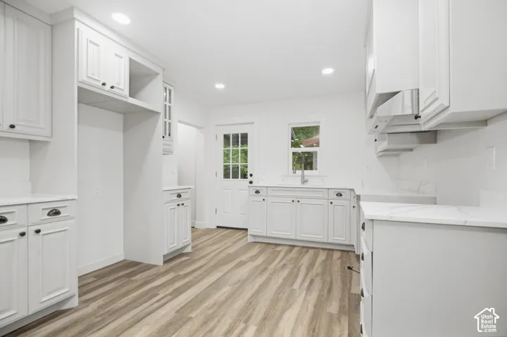 White shaker-style cabinetry, wood-finish flooring, recessed lighting, white countertops, and a white subway tile backsplash