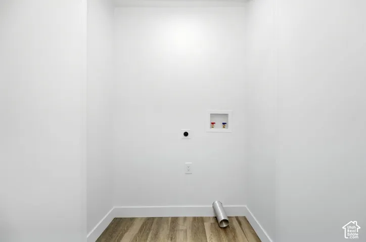Dedicated utility area featuring white walls, wood-finish flooring, and plumbing connections for appliances