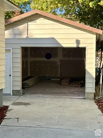 Attached garage structure with light-toned siding, a brown-toned roof, and a concrete driveway