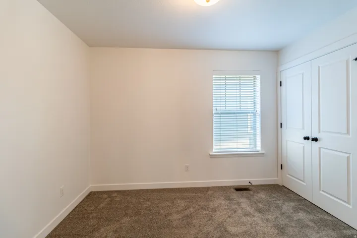 Neutral wall paint, window with horizontal blinds, textured carpet, and white bi-fold doors with black hardware