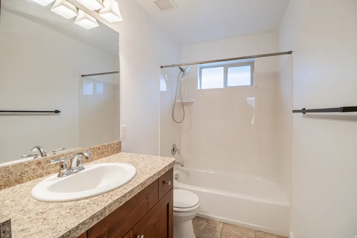 Wood-finish vanity with an integrated oval sink, speckled countertop, and chrome faucet
