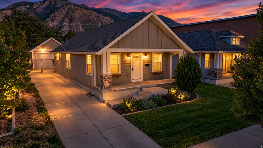 Craftsman-style exterior with stone accents, covered front porch, concrete driveway, and established landscape lighting